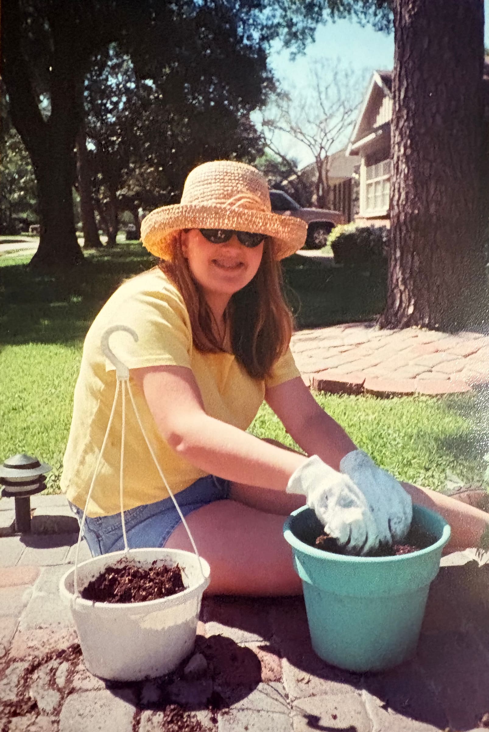 Katherine as a teenager, in a straw hat, potting hanging baskets